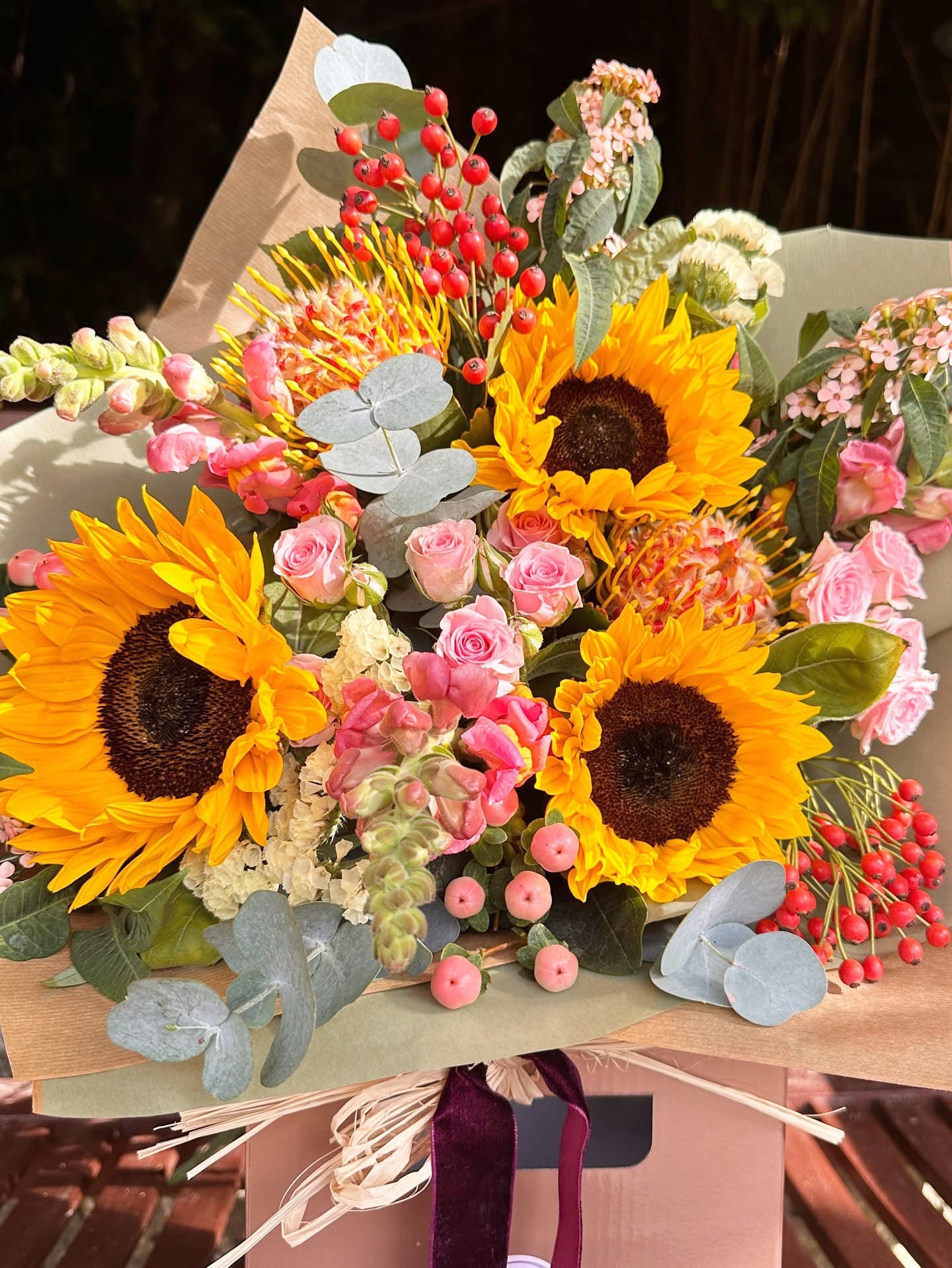 Bouquet of sunflowers, pink roses, and other flowers in a brown paper wrap.
