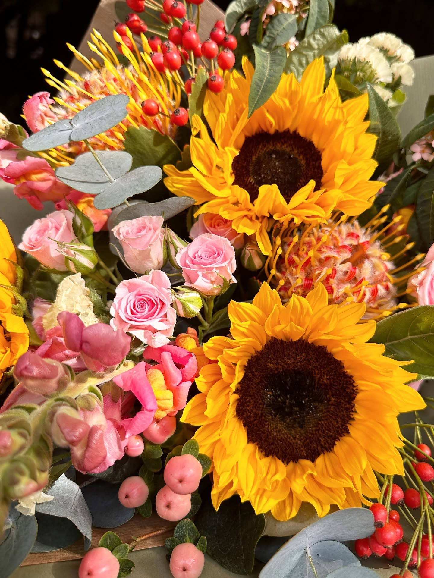 Bouquet of sunflowers, pink roses, and other flowers with greenery.