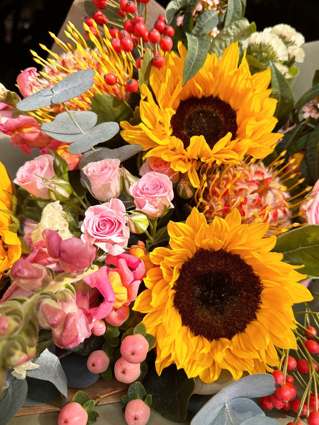 Bouquet of sunflowers, pink roses, and other flowers with greenery.
