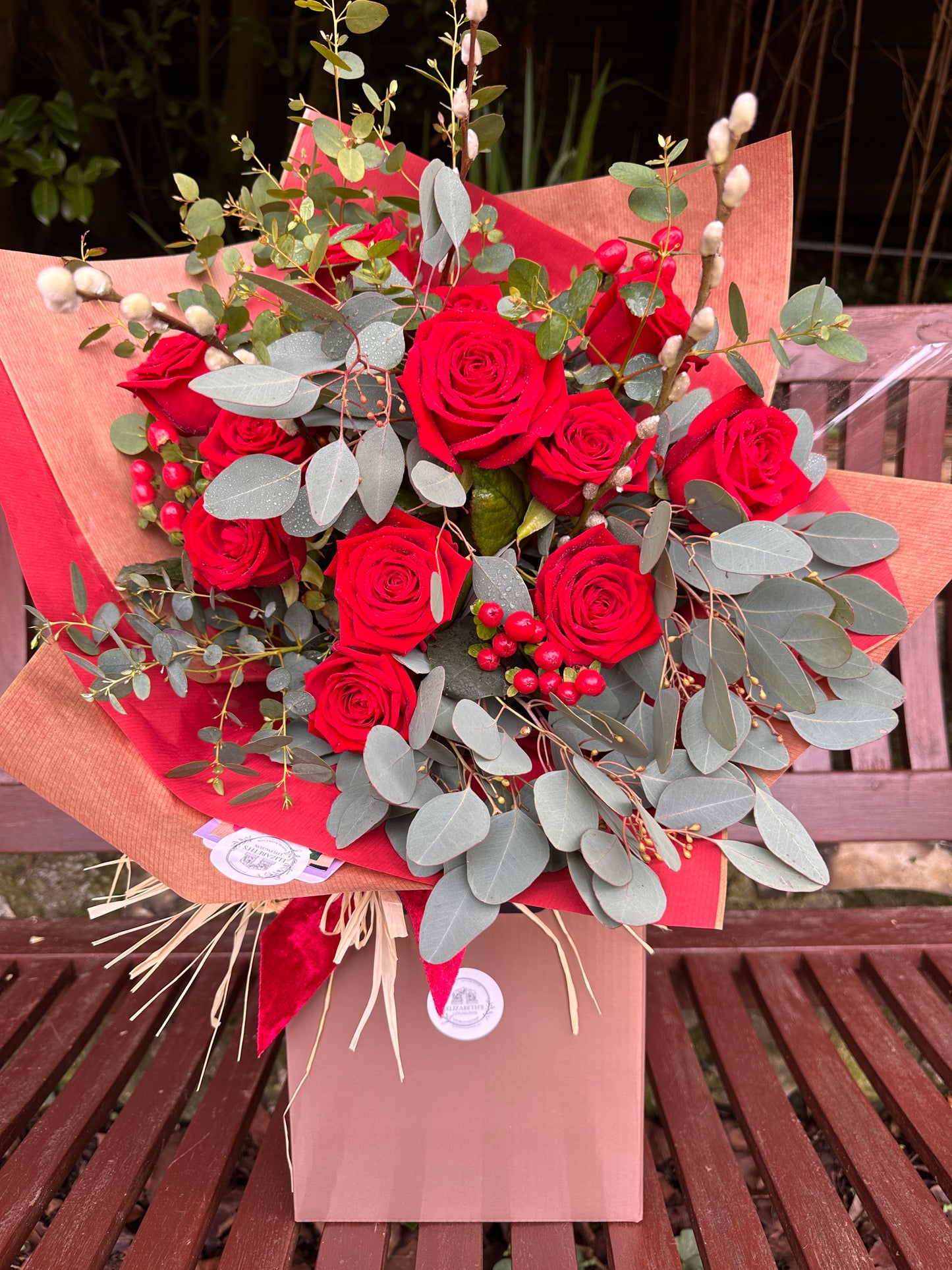 Bouquet of red roses with greenery on a wooden bench
